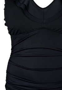 Le maillot de bain noir présente un tissu froncé, un décolleté en V et des accents volants le long des bretelles, offrant une apparence texturée.