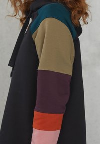 Felpa con cappuccio caratterizzata da un corpo nero e maniche multicolori (turchese, oliva, burgundy, arancione, rosa) con una texture liscia e un cordino regolabile.