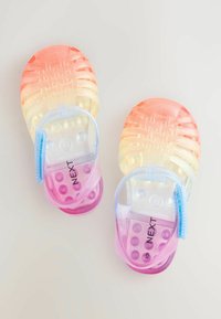 Permatomos sandalai su gradientu nuo oranžinės iki rožinės spalvos, tekstūruotu viršumi ir spalvotomis, burbuliukų formos pado dalimis. Ant šono matomas prekės ženklas.