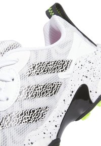 White athletic shoe with breathable mesh, black and white zigzag stripes, speckled sole, and green accents on the heel and outsole.