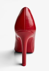 Pantofii cu toc înalt din piele lac red, cu vârf ascuțit, textură netedă și toc subțire de tip stiletto. Vizați din unghiul din spate.