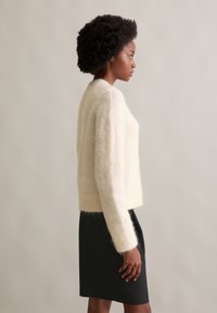 Ivory sweter z mieszanki wełny o luźnym kroju, z prążkowanymi mankietami i dołem. Zestawiony z czarną spódnicą, prezentującą miękkie, teksturowane wykończenie.