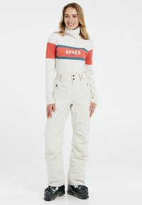 Cremfarbene Skihosen mit hoher Taille, zwei Knöpfen und seitlichen Taschen, kombiniert mit einem langärmeligen Oberteil in Weiß und Rot mit Streifen.
