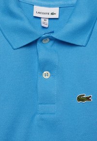 Polo tričko ve sv�ětle modré barvě z bavlny s texturovaným povrchem, se zapínáním na dva knoflíky a malým vyšitým zeleným logem krokodýla.
