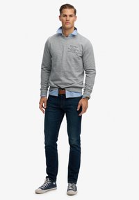 Szary sweatshirt z logo, nałożony na jasnoniebieską koszulę z kołnierzykiem. Ciemnoniebieskie skinny jeansy i granatowe trampki z białymi akcentami.