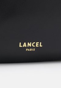 Fekete bőr anyag sima textúrával, arany betűkkel dombornyomott "LANCEL" és "PARIS" márkanevével.