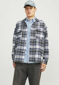Flannel skjorte i blå, hvid og sort ternet mønster, med to brystlommer, parret med en lys blå denim skjorte under.