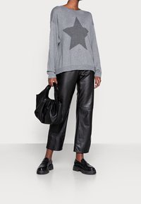 Pull gris avec un motif d'étoiles foncé, pantalon en cuir noir, sac noir et chaussures noires épaisses. Coupe décontractée et texture douce dans l'ensemble.