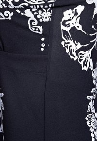 Le tissu bleu marine présente des motifs floraux blancs, une poche et une finition texturée. Le design inclut des accents décoratifs le long des bords.