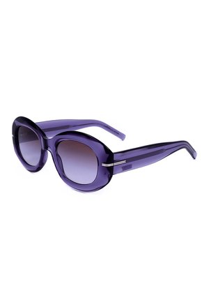 Occhiali da sole rotondi oversize viola con lenti scure sfumate e montature spesse traslucide, mostrati leggermente inclinati su sfondo bianco.