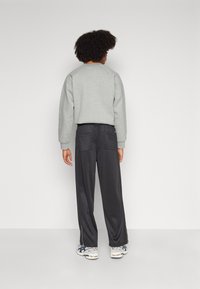 Grauer Sweatshirt mit gerippten Bündchen und Kragen, kombiniert mit schwarzen, weit geschnittenen Hosen, die zwei Gesäßtaschen und einen subtilen Glanz aufweisen.