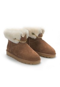 Botas de tobillo de ante marrón con un suave cuello de piel sintética blanca y acento de cadena dorada. Suela plana con agarre texturizado para tracción.