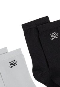 Deux paires de chaussettes de cheville, l'une noire et l'autre blanche, chacune avec un petit logo brodé près de la bordure.