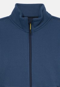 Giacca in pile blu con texture, chiusura a zip e colletto alto, dotata di un linguetta per la zip gialla.