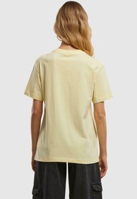 Yellow cotton t-shirt with short sleeves and a crew neck, featuring a relaxed fit and a smooth texture. Back view shows no additional details.