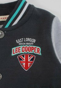 Veste gris foncé avec "East London Denim Brand Lee Cooper" brodé au-dessus d'un patch en forme de blason Union Jack, et col rayé en noir, blanc et sarcelle.