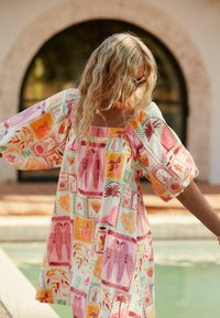 Korte mouwen, vierkante hals jurk van kleurrijke, gestippelde stof met palmbomen, vogels en bloemenpatronen in roze, oranje en groen.