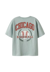 T-shirt en coton vert clair à manches courtes. Présente des graphiques rouges et blancs avec le mot "CHICAGO BASEBALL" accompagné de balles de baseball et d'accents de laurier.