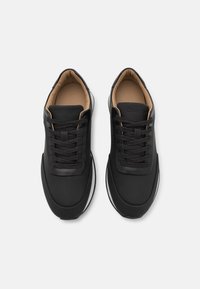 Černé sportovní boty s hladkým, matným koženým povrchem, kulatou špičkou a bílou gumovou podrážkou. Disponují černými tkaničkami a značkovým jazykem.