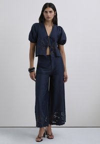 Conjunto de satén azul marino de dos piezas que incluye un top corto con mangas abullonadas y bordes de encaje, y pantalones de pierna ancha con recortes y detalles bordados.