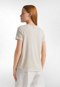 Beige t-shirt med korta ärmar och rund halsringning, mjuk bomullstextur och en liten tygögla bak.
