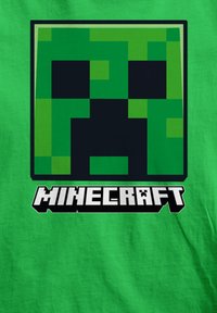 Camiseta verde con un diseño de cara de creeper verde pixelada centrada sobre la palabra "MINECRAFT" en letras mayúsculas blancas y en negrita.