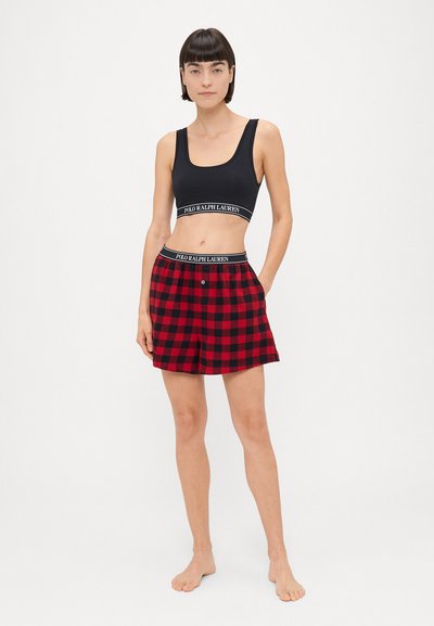 Sort crop top med brede stropper og logobånd, parret med rød og sort ternede shorts med knap og elastisk talje.