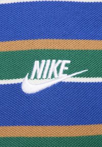 Logo Nike blanc brodé sur un tissu tricoté à rayures bleues, vertes, beiges et blanches.