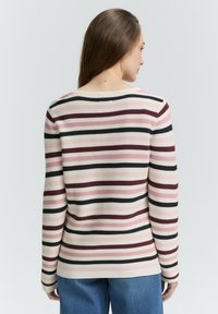 Juostuotas megztinis su rilku tekstūra, turintis rožines, kremines ir juodas juostas. Platus iškirpimas ir ilgomis rankovėmis. Dėvimas su mėlynomis džinsomis.