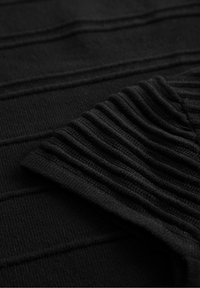 Svart stickad tyg med texturerade horisontella ränder och samlad detalj på ena kanten, som visar en mjuk, elastisk textur.