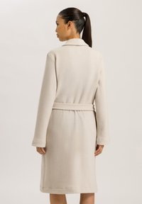 Robe beige in tessuto morbido e testurizzato, con maniche lunghe, collo a camicia e una cintura in vita, che arriva fino a metà polpaccio.