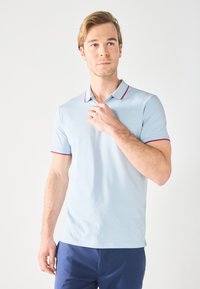 Lys blå polo skjorte med kontrastfarge i rød på kragen og ermet, laget av en glatt og pustende stoff. Standard passform med korte ermer.