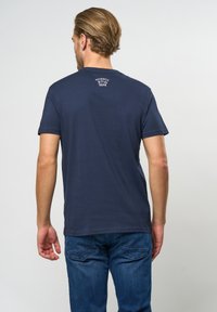 Navyblaue Baumwoll-T-Shirt mit kurzen Ärmeln, das einen kleinen weißen Grafikdruck auf dem oberen Rücken zeigt. Der Stoff sieht weich und glatt aus.