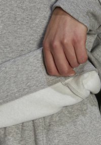 Main soulevant l'ourlet d'un sweat-shirt gris pour montrer sa couche intérieure en polaire blanche et douce.