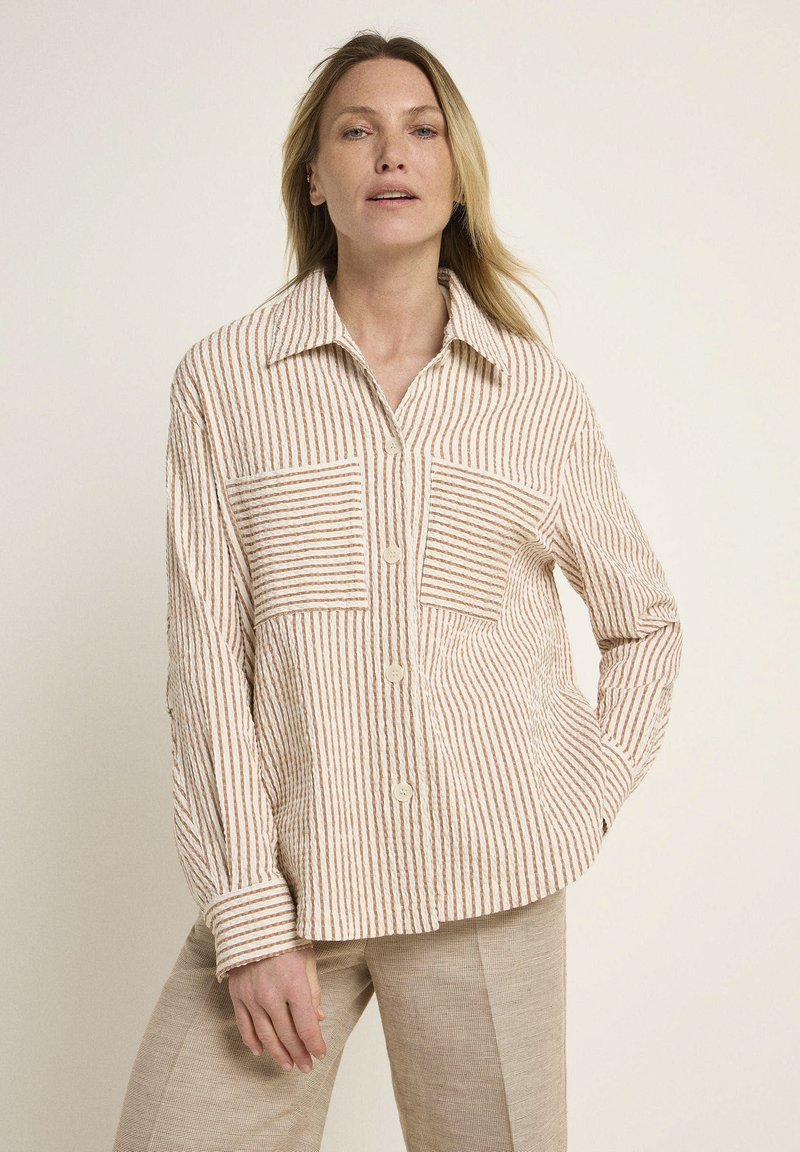 Striped button-up shirt in beige with horizontal and vertical lines; features two chest pockets and a classic collar. Textured fabric.