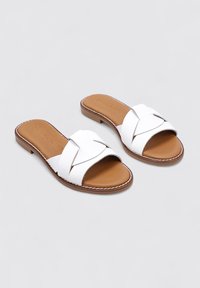 Sandalias deslizantes de cuero blanco con diseño de tira entrecruzada, plantilla acolchada marrón y suela plana marrón claro con detalles de costura.