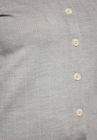 Cardigan gri deschis, cu caneluri, fabricat dintr-un material moale, cu cinci nasturi crem. Prezintă dungi verticale și un aspect texturat.