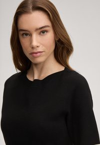 Μαύρο πλεκτό πουλόβερ με στρογγυλή λαιμόκοψη και κοντά μανίκια. Το ύφασμα είναι λείο με διακριτική υφή και ριμπ λεπτομέρειες στον γιακά.