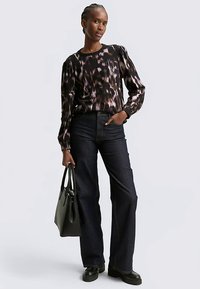 Top de manga larga con estampado negro y rosa, con cuello redondo, combinado con jeans acampanados de mezclilla oscura de cintura alta y un bolso tote negro.