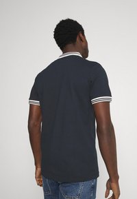 Navy blue polo shirt with white striped collar and sleeve cuffs, short sleeves, and a fitted design. Plain texture, no visible patterns.