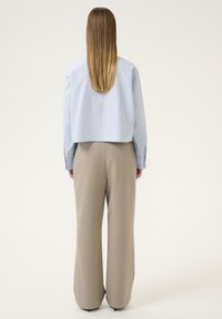 Lichtblauw cropped shirt met lange mouwen, gecombineerd met beige wijde broek. De broek heeft een nette uitstraling met subtiele textuur en plooien.
