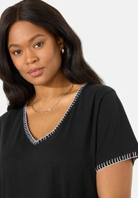 Černé tričko s výstřihem do V a krátkým rukávem s bílým kontrastním prošíváním podél výstřihu a lemů rukávů. Hladká textura, casual design.