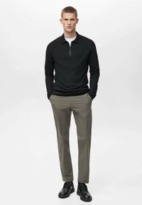 Pullover nero con zip, tessuto teksturizzato, abbinato a pantaloni grigi chiari. Scarpe nere completano l'outfit. Design minimalista senza motivi.