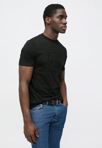 Μαύρο βαμβακερό μπλουζάκι με ανάγλυφο σχέδιο φιγούρας με γυαλιά ηλίου. Συνδυάζεται με μπλε τζιν και μαύρη ζώνη. Μινιμαλιστικό στυλ.