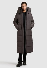 Long, padded dark gray coat with a high collar and hood. Features a front zipper and pockets, shown on a model against a neutral background.