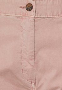 Tessuto rosa chiaro con una texture liscia, caratterizzato da un piccolo bottone marrone e cuciture visibili vicino alla vita e all'area delle tasche.