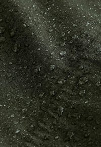 Tessuto verde scuro idrorepellente con una superficie texture, caratterizzato da gocce d'acqua sparse, evidenziando l'efficacia del materiale.