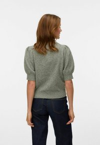 Maglione verde a maglia con maniche corte a sbuffo, orlo a coste, tessuto testurizzato, indossato con jeans a vita alta blu scuro.