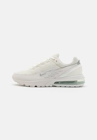 Nike Air Max-sneaker i off-white mesh med silverdetaljer, hälinlägg för luftdämpning och texturerad gummisula. Minimalistisk design med perforeringar.