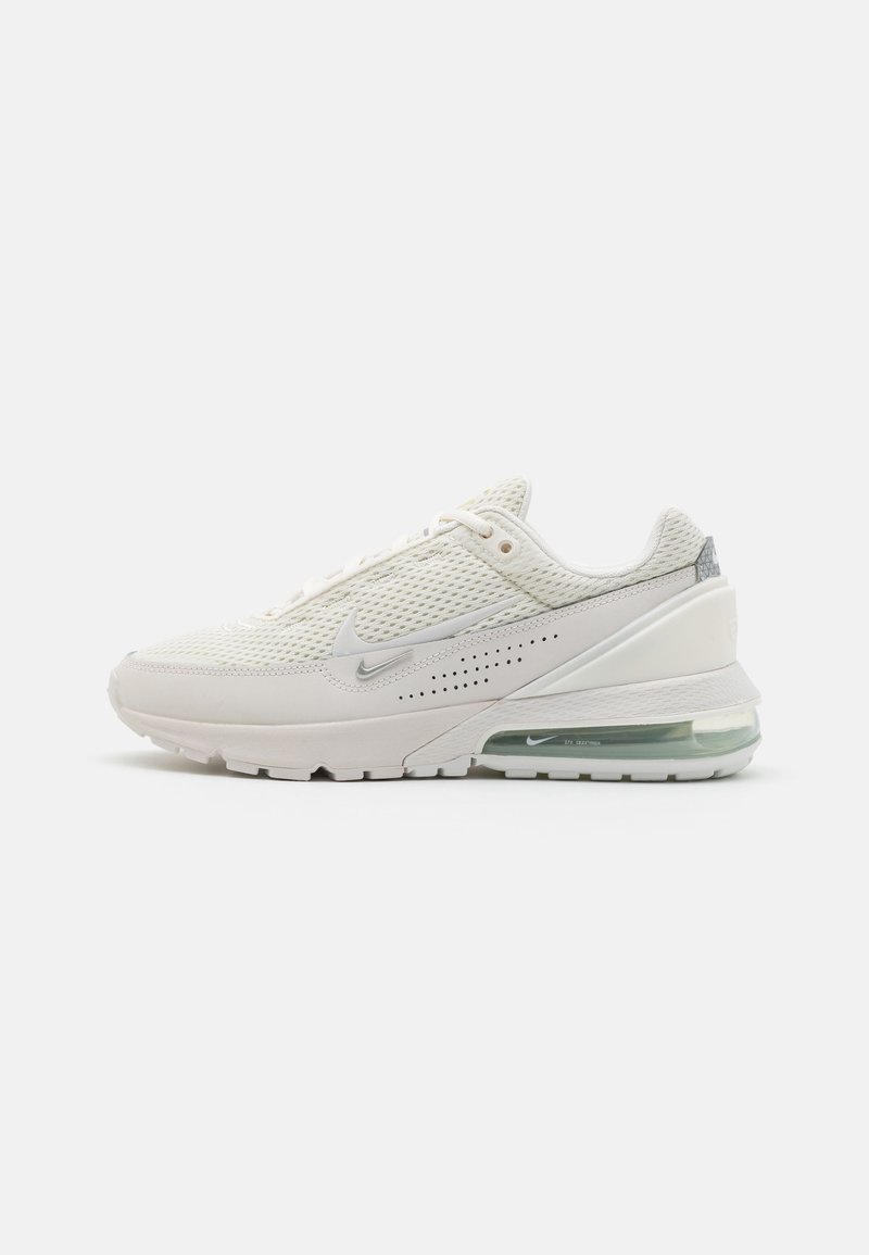 Nike Air Max-sneaker i off-white mesh med silverdetaljer, hälinlägg för luftdämpning och texturerad gummisula. Minimalistisk design med perforeringar.